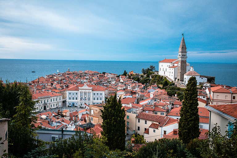 Coastal view of Slovenian Riviera with red-roofed houses and a church in the distance.