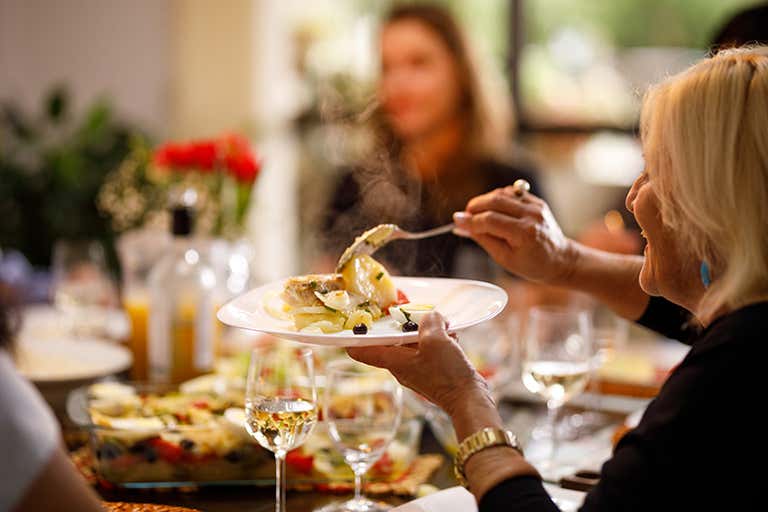 A cheerful dining scene with a woman enjoying a plate of steaming food, surrounded by glasses and vibrant table decor.