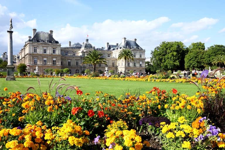 Os Jardins de Luxemburgo, em Paris, em junho, repletos de flores coloridas, enquanto o palácio se destaca elegantemente ao fundo.