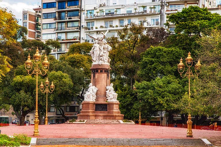 Monument with white marble statues and ornate lampposts in Buenos Aires plaza.