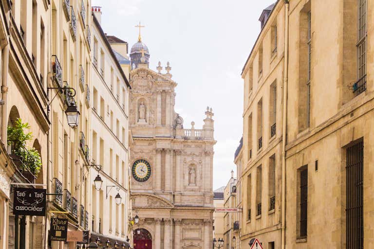 Saint-Paul-Saint-Louis Baroque facade with ornate carvings, clock and dome peeking above narrow Marais district street