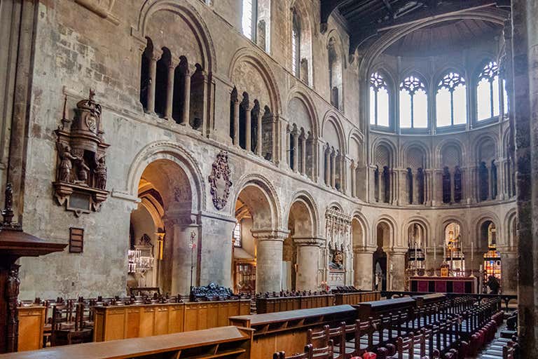 Interior of St. Bartholomew the Great with ancient stone arches, wooden choir stalls and Romanesque architecture in soft light