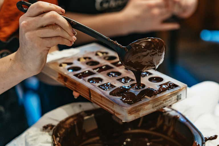 A person pouring melted chocolate into a mold using a ladle.