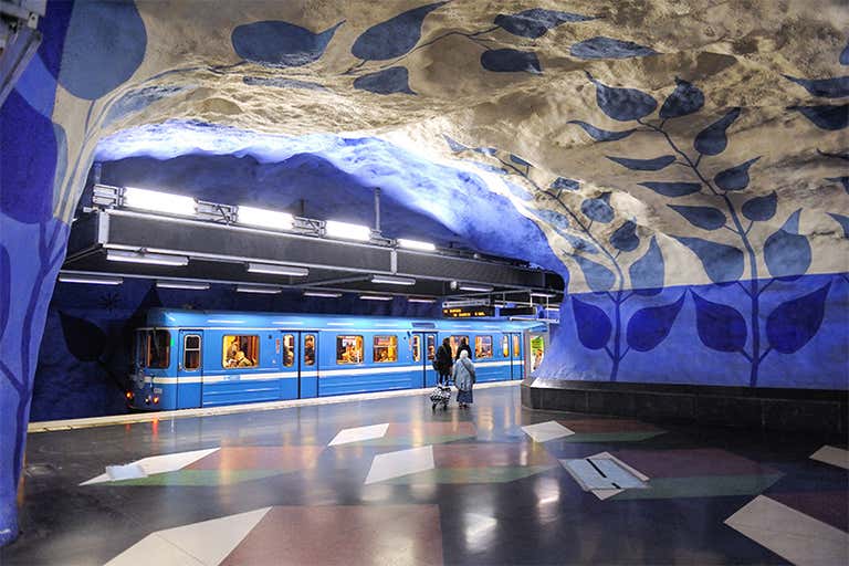Um trem azul na estação T-Centralen com padrões artísticos de folhas azuis nas paredes e no teto.
