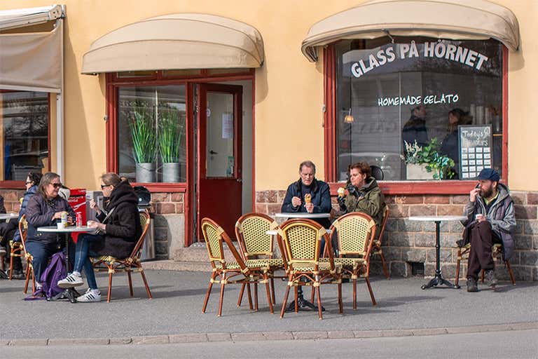 Pessoas sentadas do lado de fora de uma loja de gelato chamada Glass På Hörnet saboreando sorvete.
