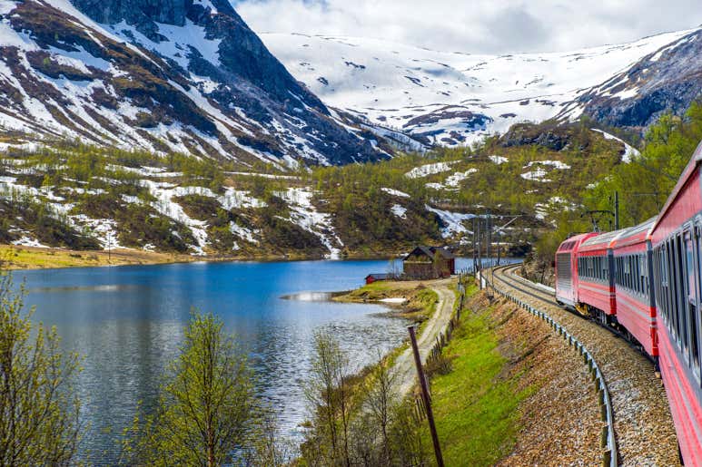 Train traveling beside a mountain lake on the Bergensbanen railway in Norway.