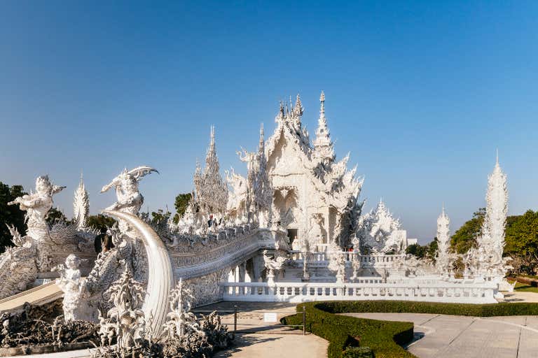 Ornate white temple with intricate spires and mythical sculptures glows in sunlight, showcasing one of Thailand's most unique architectural marvels