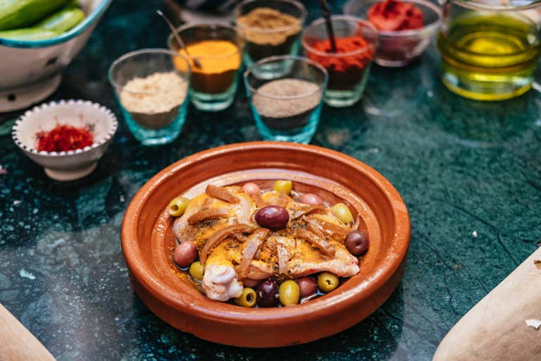 Un tagine tradicional marroquí con pollo y aceitunas, rodeado de tazas de especias.