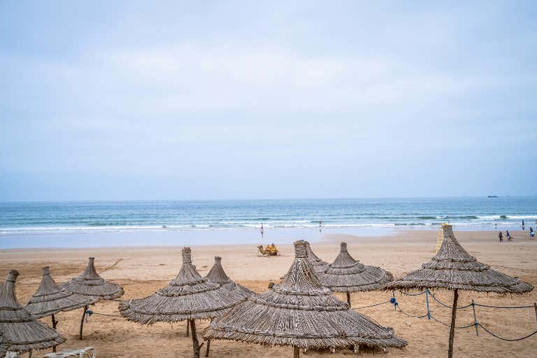 Sombrillas de paja frente al mar en la orilla arenosa de la playa de Agadir.