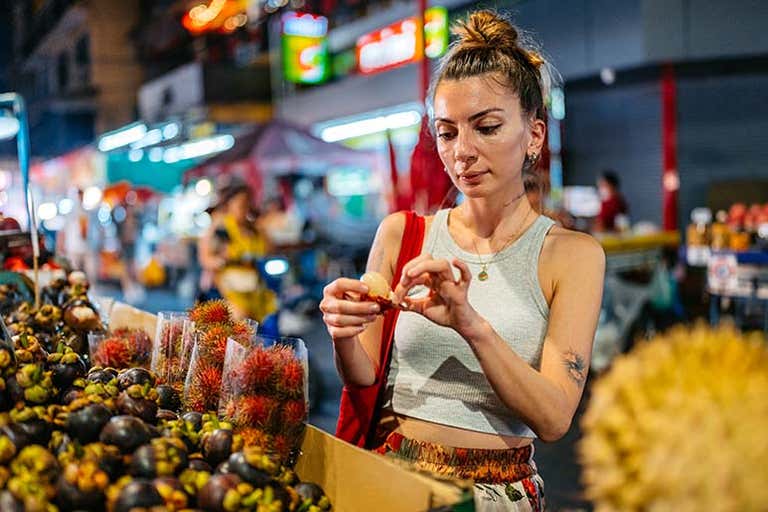 Girl browsing a bustling fruit market at night, with tropical fruit stalls and neon signs/