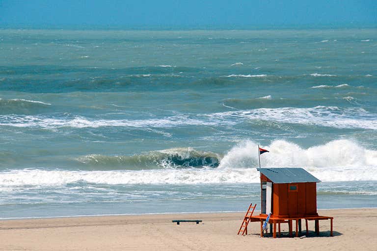 Uma cabana de salva-vidas em uma praia de areia com ondas ao fundo.