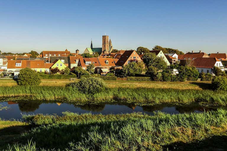 A scenic view of the town of Ribe, Denmark, with its historic buildings and a river in the foreground.