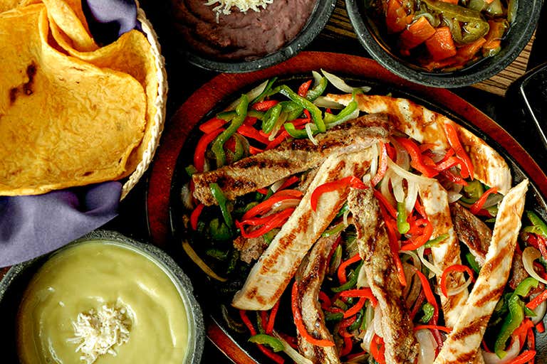 Grilled chicken and beef fajitas with sautéed peppers and onions, served with tortillas, guacamole and beans.
