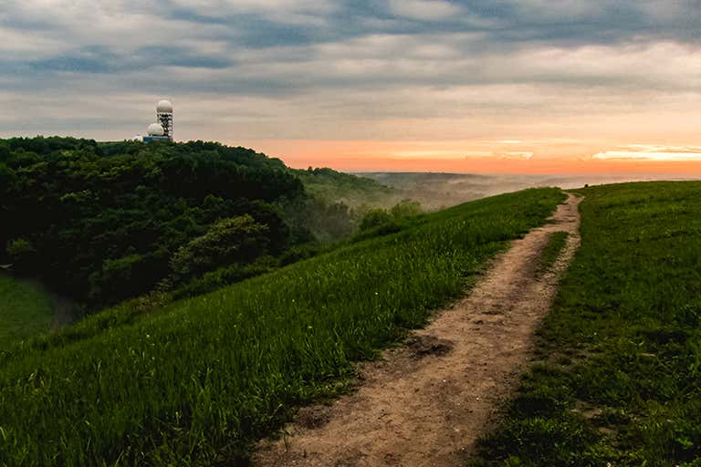 A scenic view of a path leading to a sunrise over a lush green landscape.
