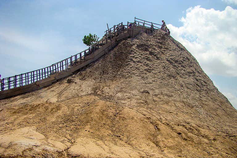 El Totumo Mud Volcano with stairs leading to the top under a blue sky.