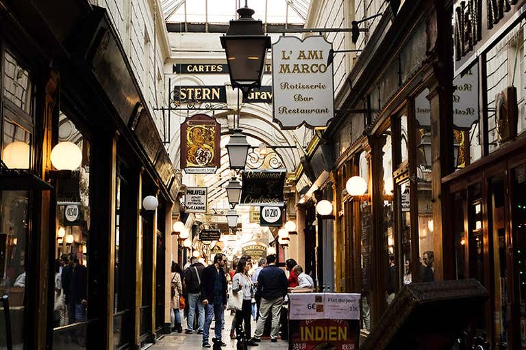Historic Parisian arcade with vintage shop signs, lanterns, and people strolling through the covered passage.