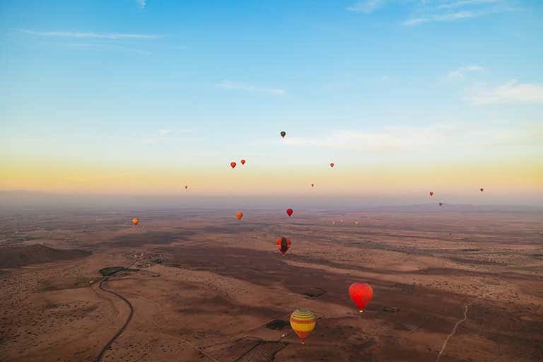 Globos aerostáticos flotando sobre un paisaje desértico al amanecer.