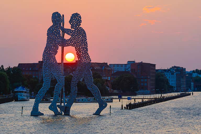 Sunrise over the Spree River with the Molecule Man sculpture in Berlin.