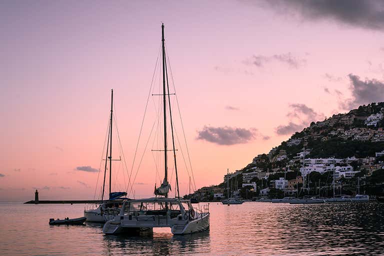 A serene sunset view of Port d'Andratx with sailboats on the water.