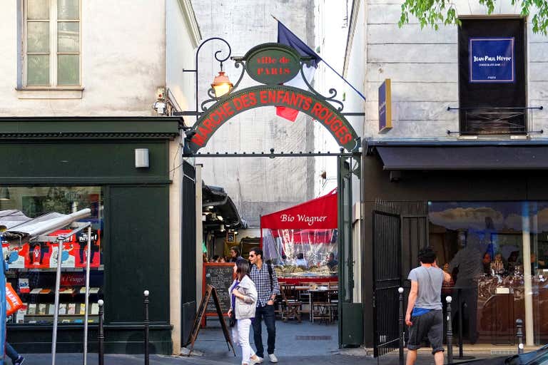 Entrance to Marché des Enfants Rouges in Paris, featuring a historic archway, storefronts, and outdoor dining areas.