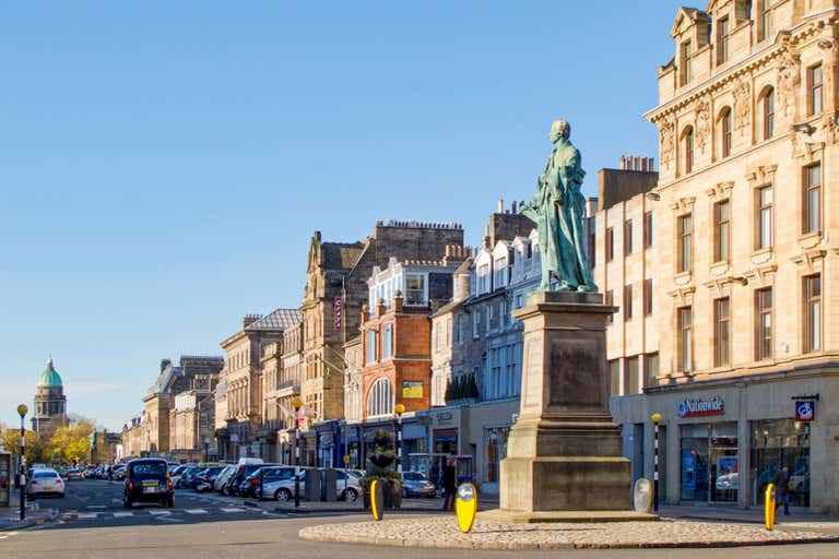 A street in Edinburgh with a statue and historic buildings.