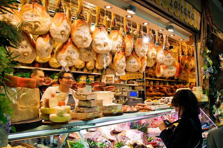 A bustling Italian deli with hanging cured meats and a variety of cheeses on display.