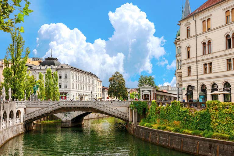 Historic Triple Bridge spans Ljubljana's emerald river, with ornate white buildings and baroque architecture creating a must-see Slovenia destination