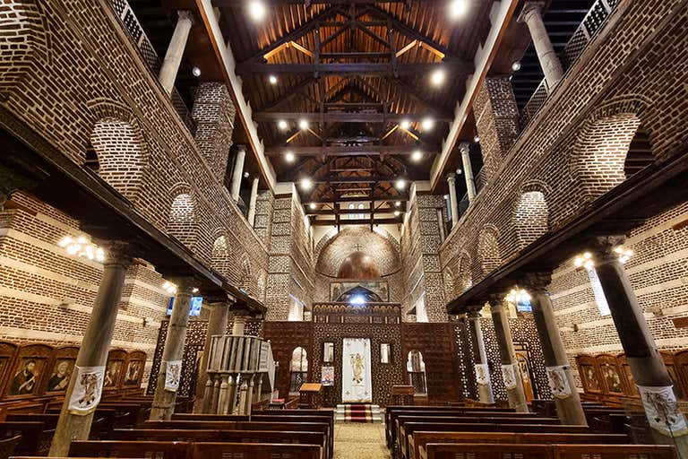 Interior of a historic church in Cairo, Egypt, featuring ornate wooden beams, brick arches, and religious icons.
