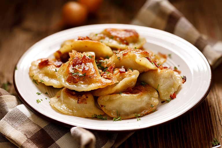 Prato de pierogi polonês coberto com cebola e salsa em uma mesa de madeira.