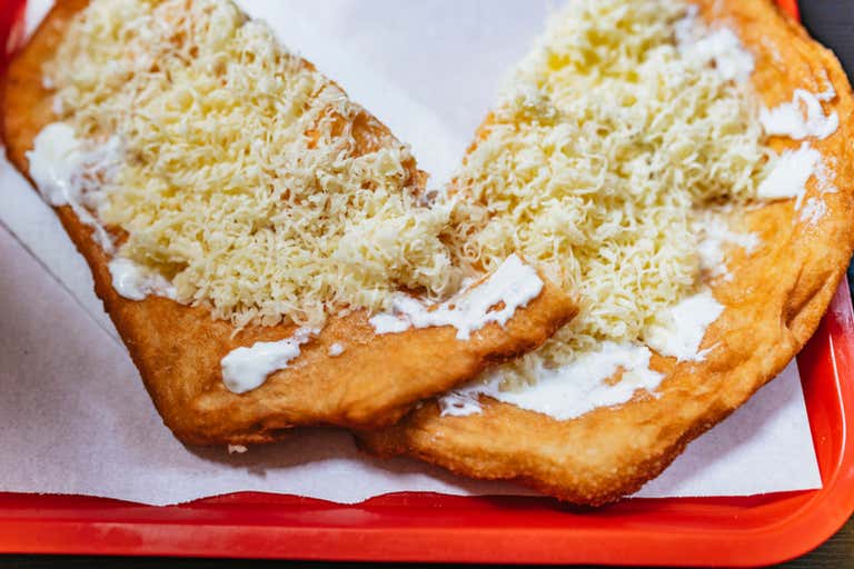 A traditional lángos topped with cheese and sour cream on a red tray