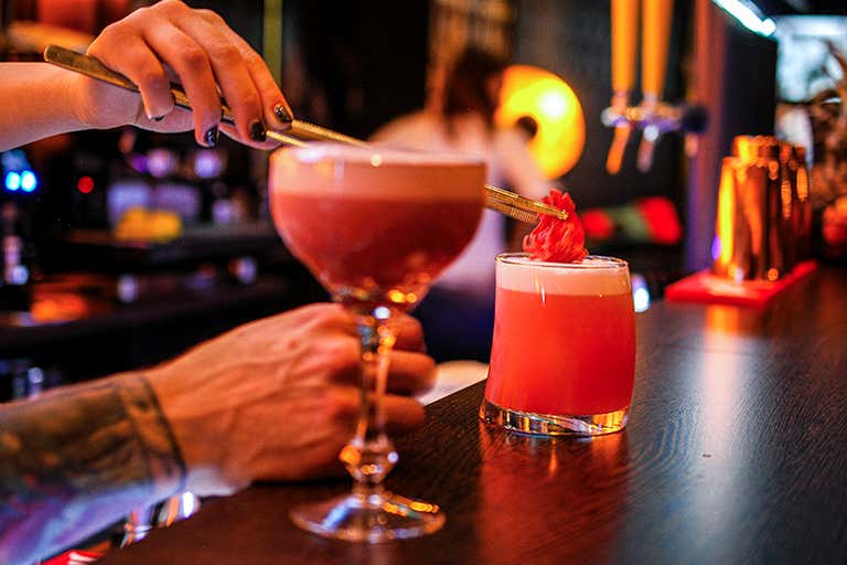 Een barman plaatst een garnering op een robijnrode cocktail