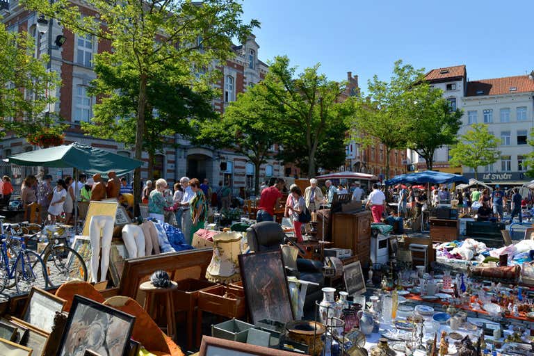 A bustling outdoor flea market with various antiques and people browsing under a clear blue sky.