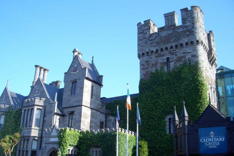 Clontarf Castle Hotel con muros cubiertos de hiedra y banderas en la entrada.