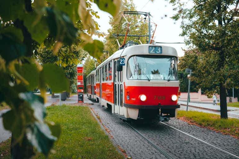 Um bonde vermelho e branco passando entre árvores em Praga.