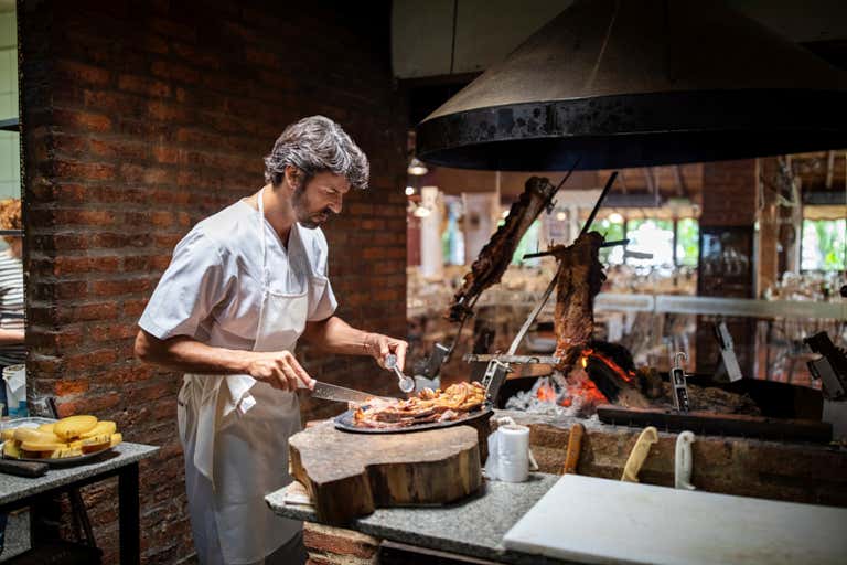 Um chef preparando o tradicional churrasco argentino em um ambiente rústico.