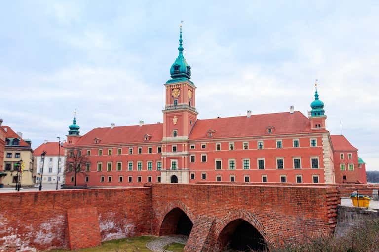 O Castelo Real em Varsóvia, com paredes de tijolos vermelhos, cúpulas verdes e uma torre de relógio.