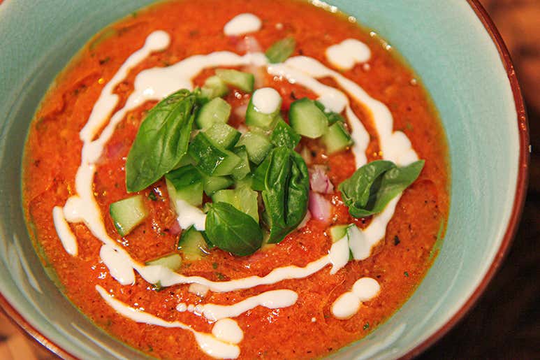 A bowl of gazpacho garnished with cucumber, basil, and cream