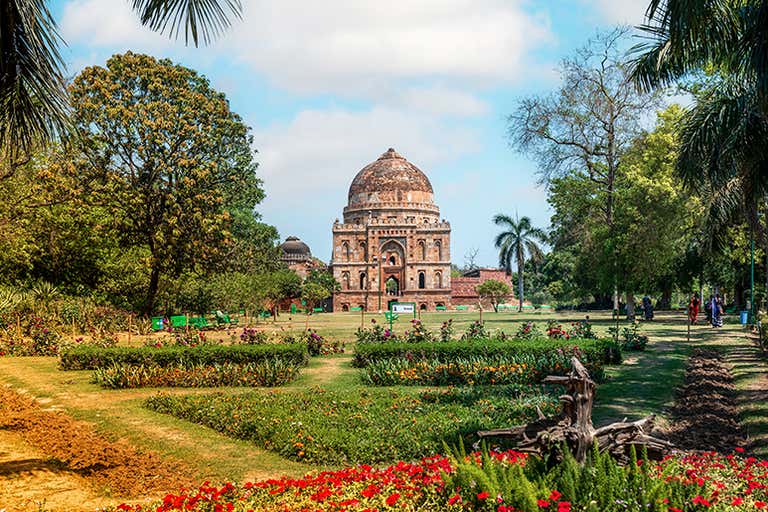 Um túmulo histórico cercado por jardins e árvores exuberantes em Nova Délhi.