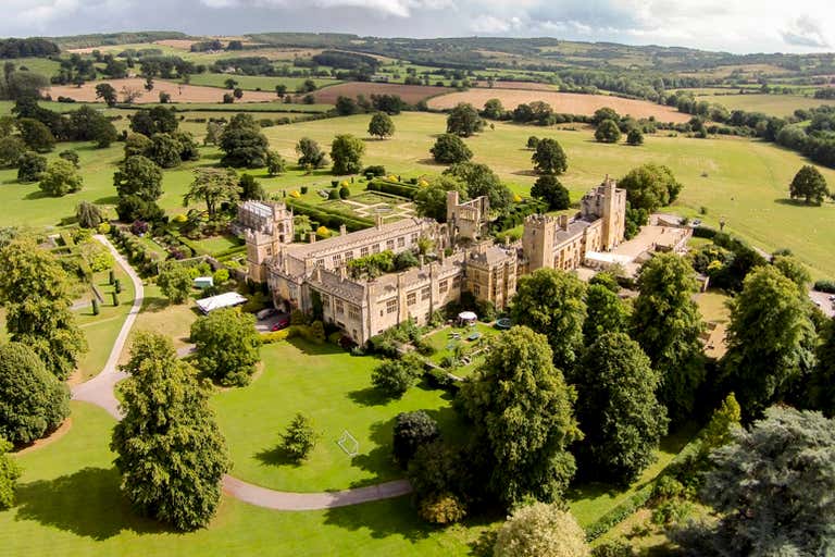 Aerial view of Sudeley Castle surrounded by lush greenery and fields.