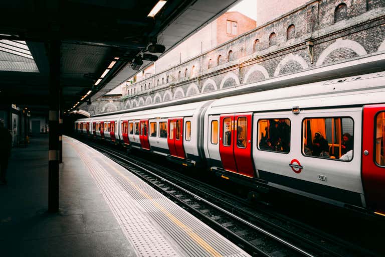 A London Underground train at a station platform with brick arches in the background.