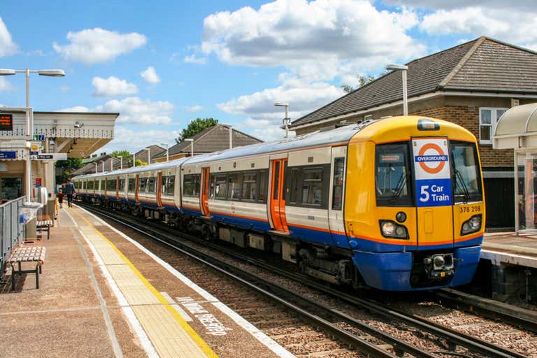 A London Overground train at a station on a sunny day.