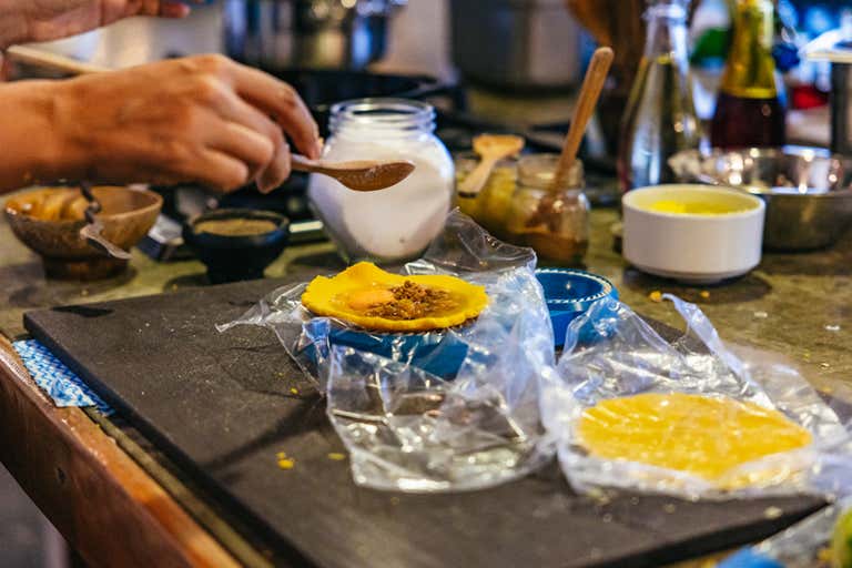 Hands preparing traditional Colombian food during a cooking class, with ingredients and tools on a wooden counter.