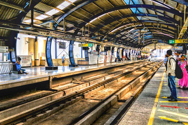 Uma plataforma movimentada em uma estação de metrô de Nova Délhi com pessoas esperando.