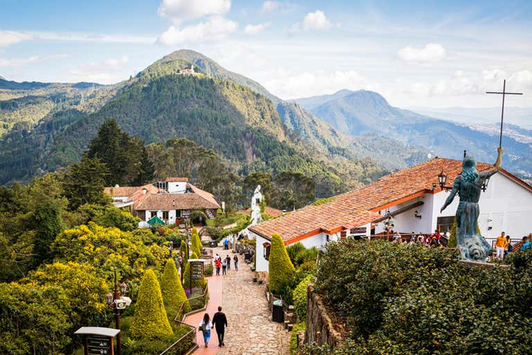 Scenic view of Monserrate in Bogotá, featuring lush green mountains, colonial-style buildings, and religious statues.