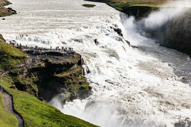 Una gran cascada con turistas en un mirador cercano.