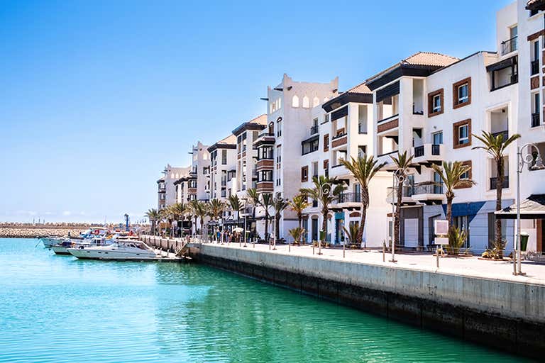 Edificios modernos se alinean en el puerto deportivo de Agadir, con yates atracados en el agua azul claro.
