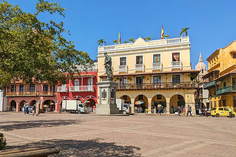 A sunny day at Plaza de los Coches in Cartagena with colorful colonial buildings and a statue.