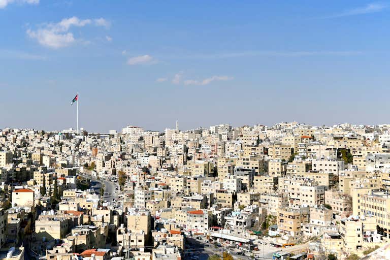 Panoramic view of Amman cityscape with densely packed beige buildings and a flag flying in the distance.