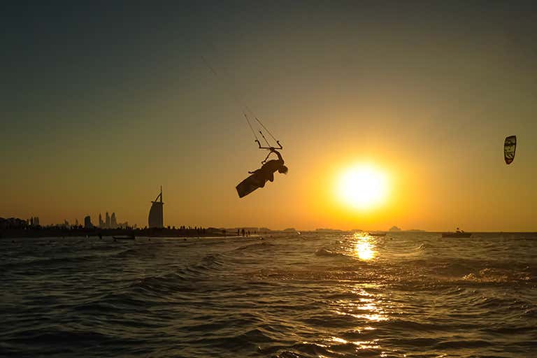 Een kitesurfer maakt een sprong tegen de achtergrond van een zonsondergang in Dubai met de Burj Al Arab op de achtergrond.