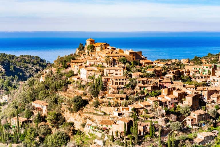 A panoramic view of Deià, Mallorca, showcasing its terraced stone houses nestled in the Tramuntana mountains.